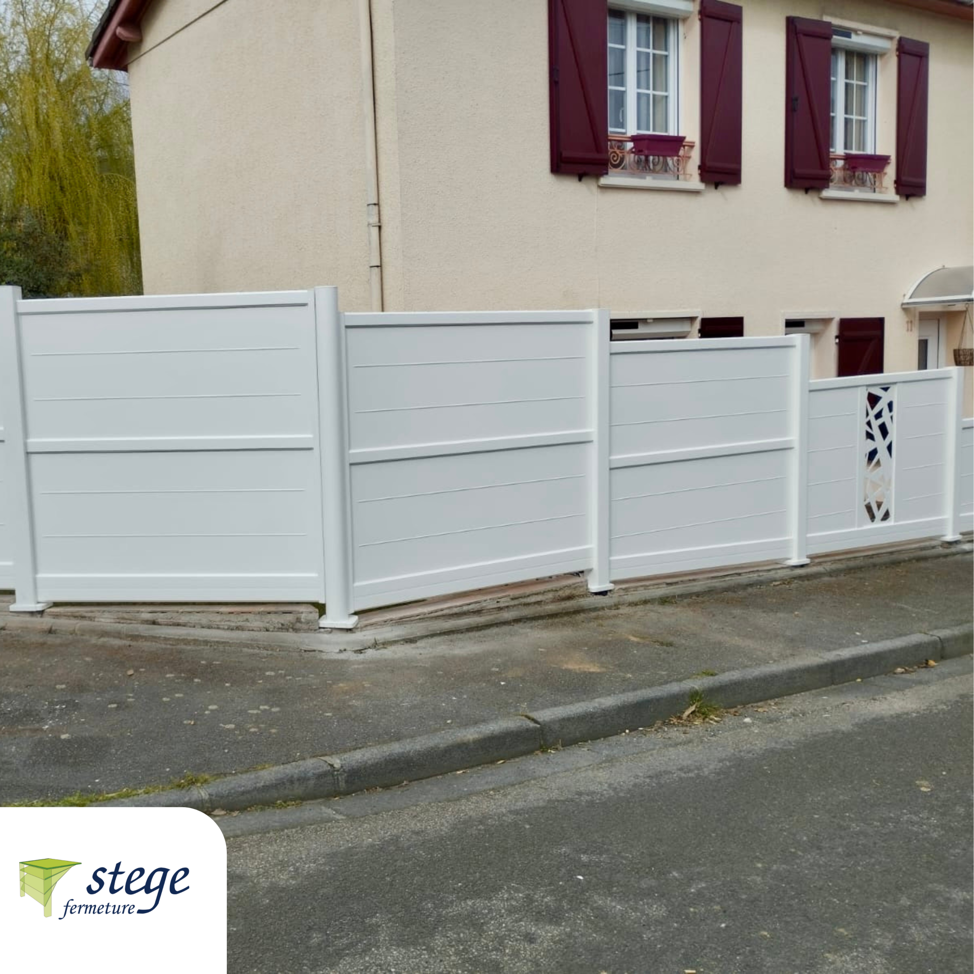 Clôture blanche préservant l'intimité d'une maison beige aux volets bordeaux, à un coin de rue