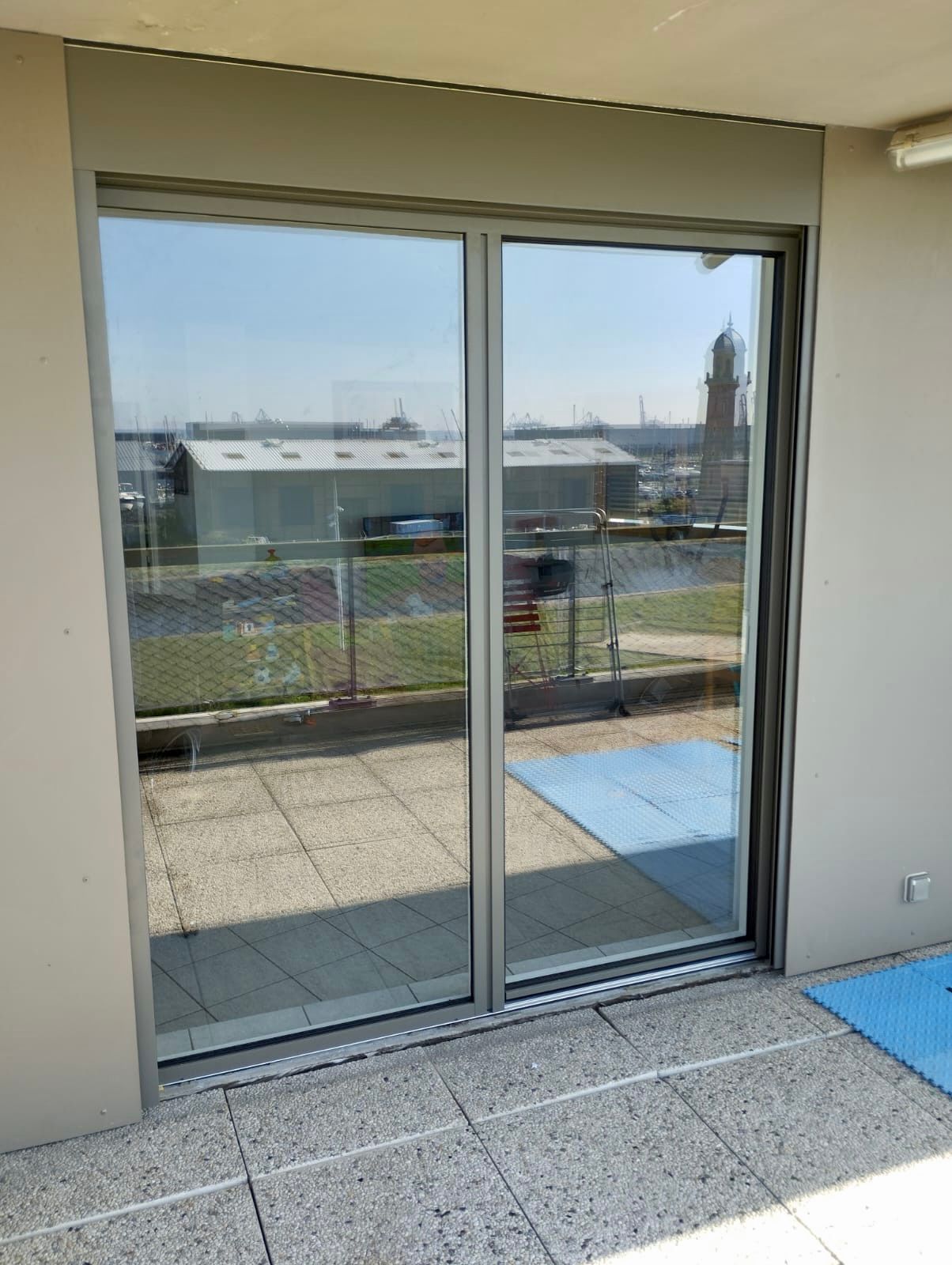 Porte coulissante en verre donnant sur un balcon avec rambarde métallique et vue sur la ville.