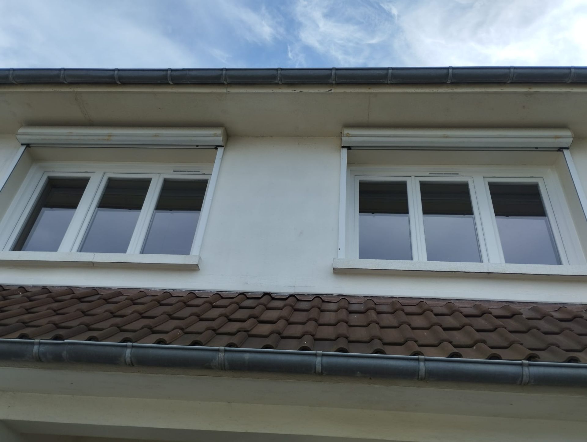 Façade de maison blanche avec deux fenêtres et un toit de tuiles sous un ciel bleu