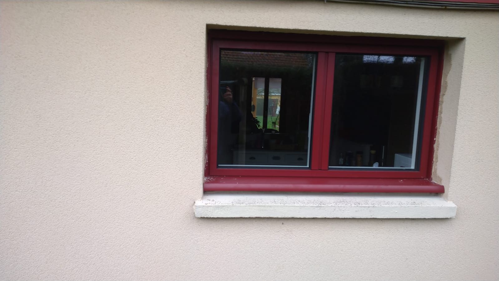 Fenêtre à cadre rouge dans un mur en stuc beige avec un appui blanc