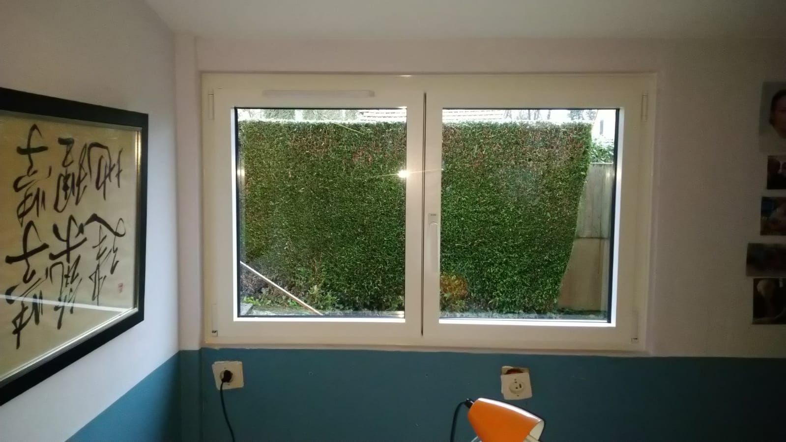 Petite pièce avec une fenêtre donnant sur les arbres, murs bas bleus et œuvre d'art encadrée sur la gauche.