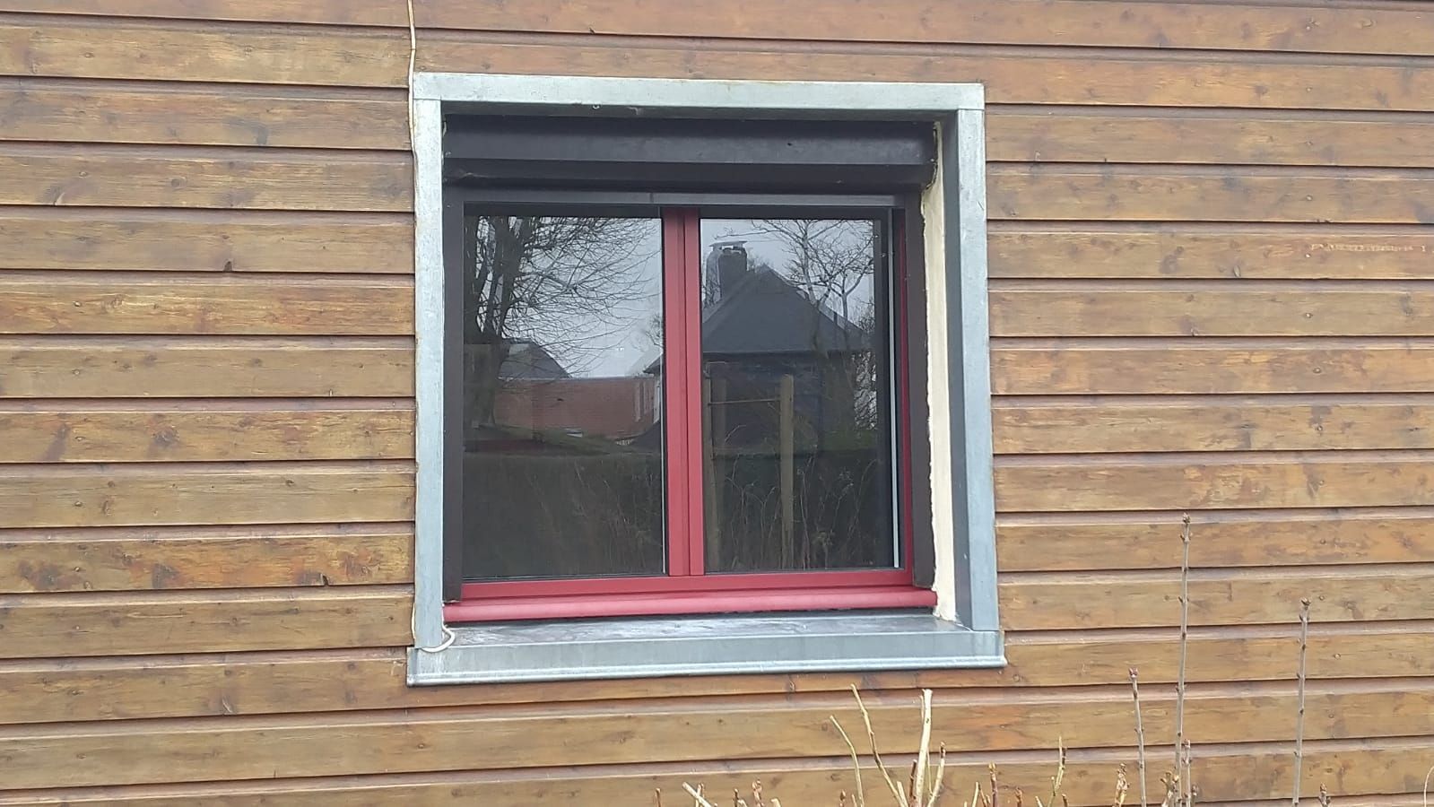 Fenêtre à cadre rouge sur un bâtiment en bois avec des finitions grises.