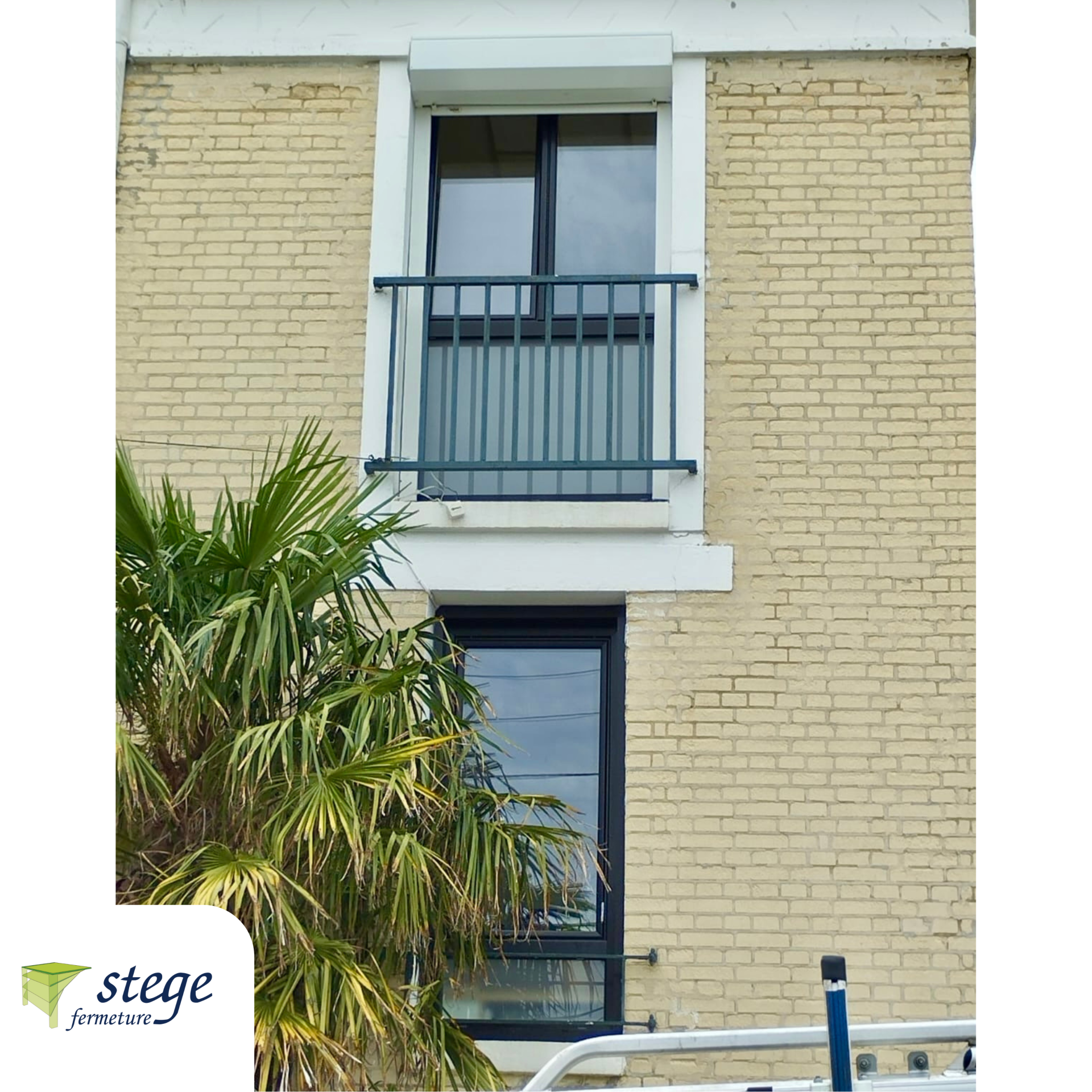 Façade d'un immeuble en briques jaunes avec deux fenêtres, une balustrade de balcon bleue et des palmes devant.