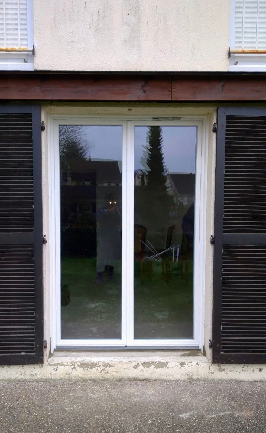 Porte-fenêtre coulissante en verre entre des volets noirs sur la façade d'un bâtiment.