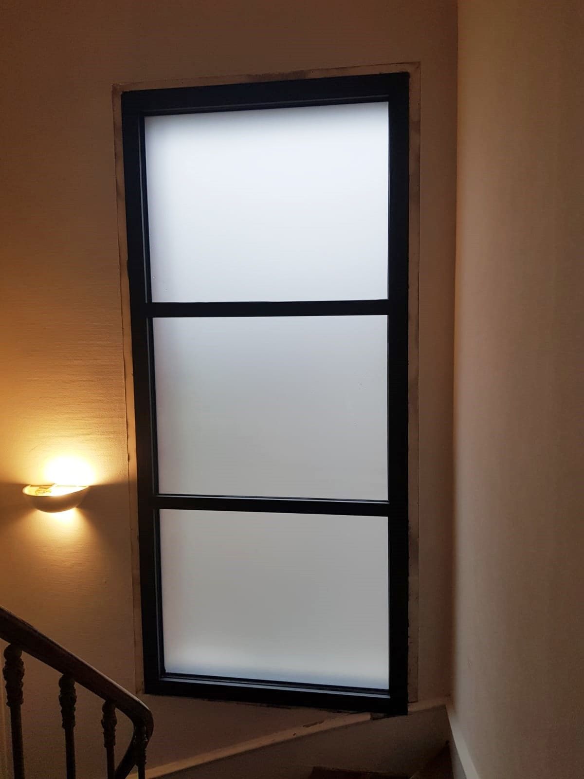 Palier d'escalier avec une grande fenêtre dépolie et une applique murale éclairée sur des murs beiges