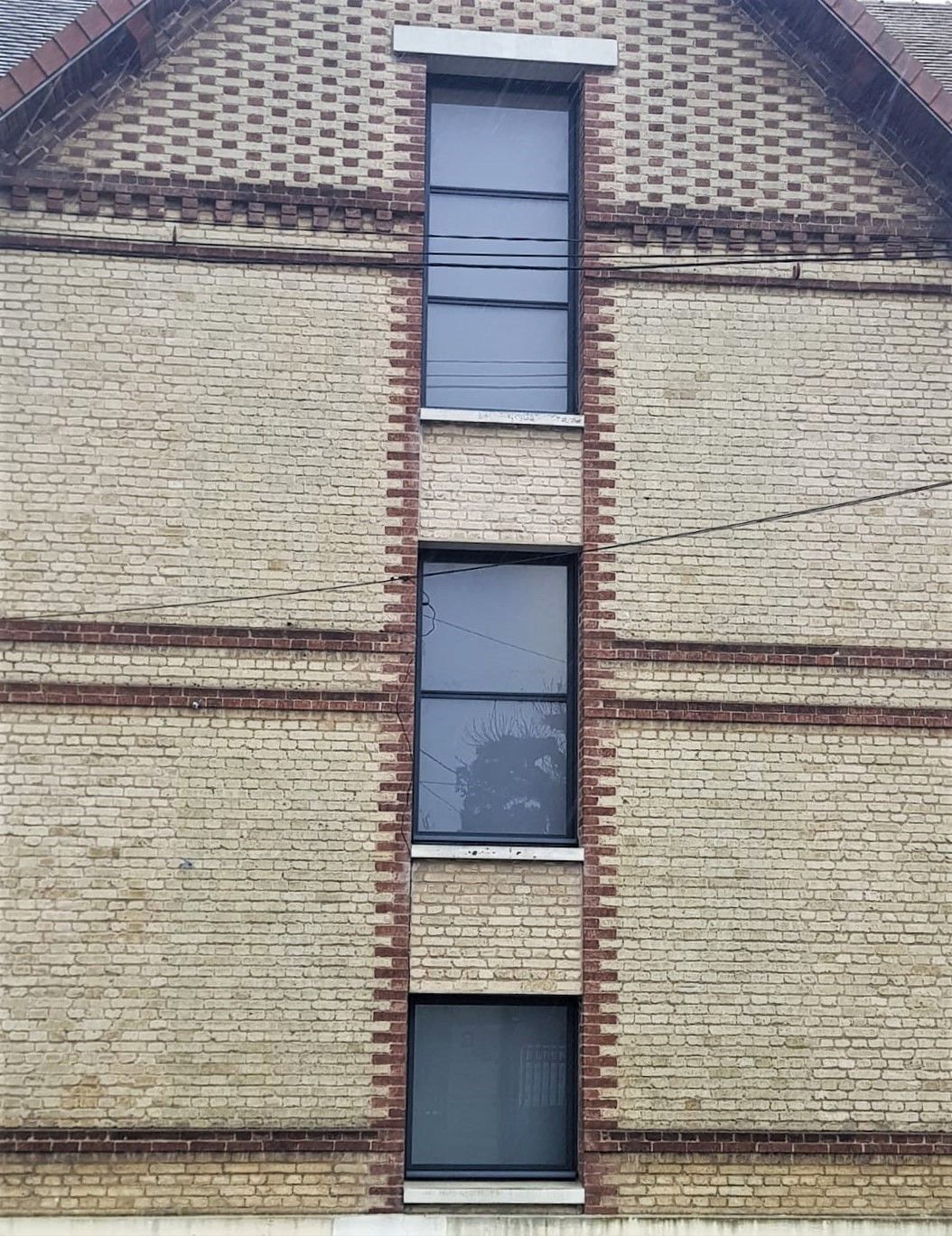 Façade en briques avec fenêtres verticales étroites et ornementation en briques sur la toiture