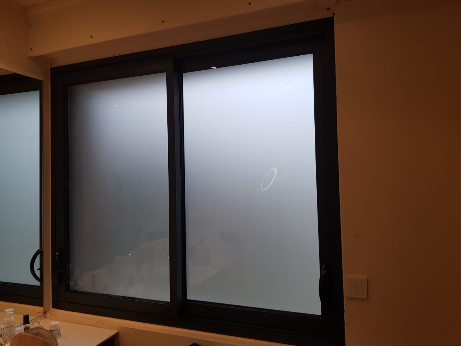 Fenêtre coulissante en verre dépoli à cadre noir dans une pièce faiblement éclairée