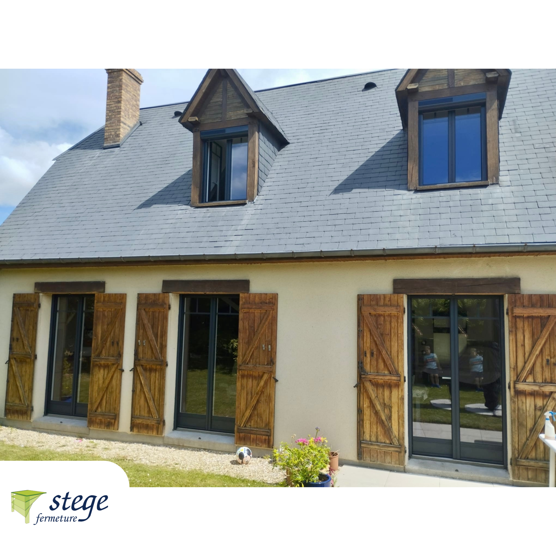 Maison en pierre avec toit d'ardoise grise, lucarnes et volets en bois par une journée ensoleillée