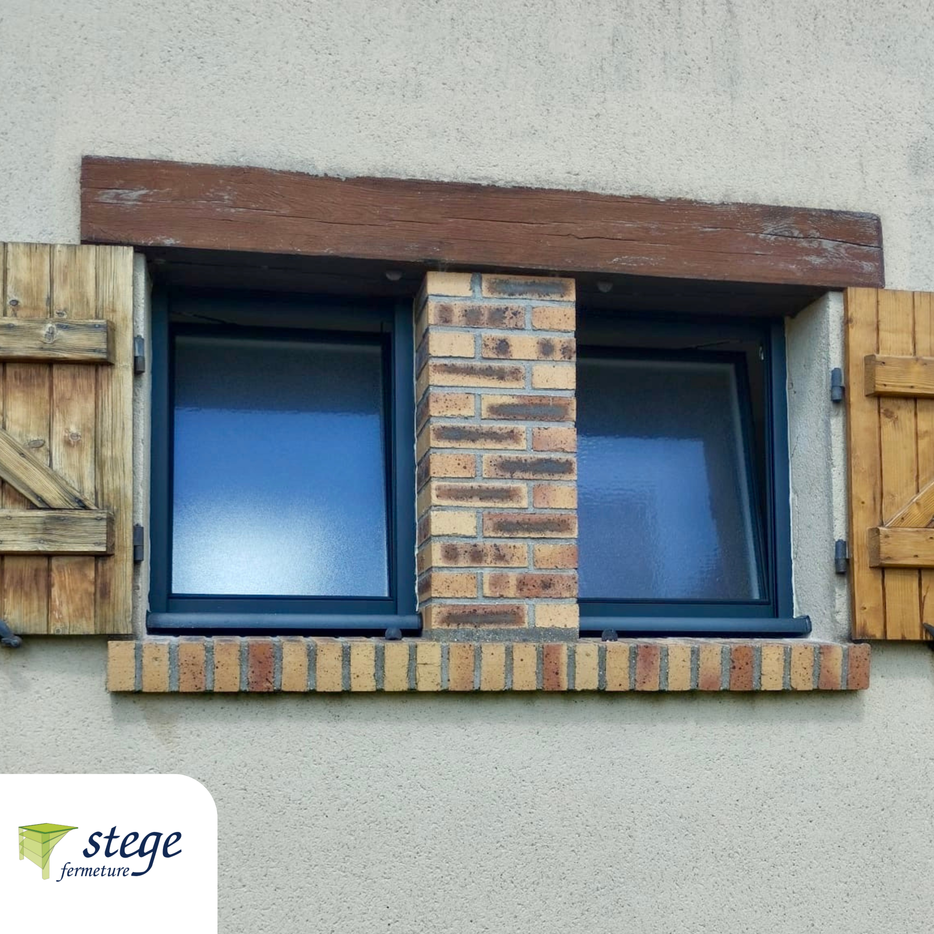 Petite fenêtre en briques avec vitres teintées bleutées, cadre sombre et volets en bois sur un mur en stuc