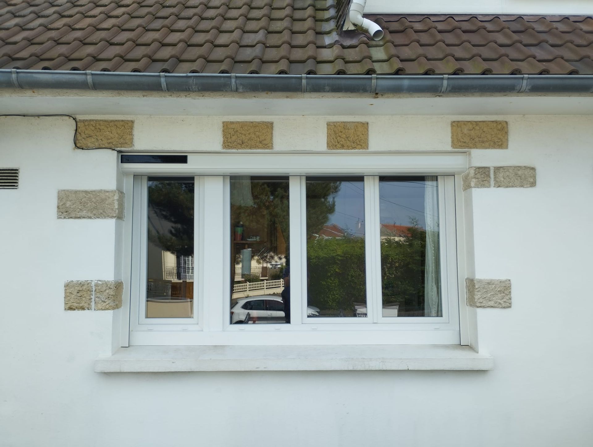 Fenêtre d'une maison blanche avec volets blancs et accents de pierre sous un toit de tuiles