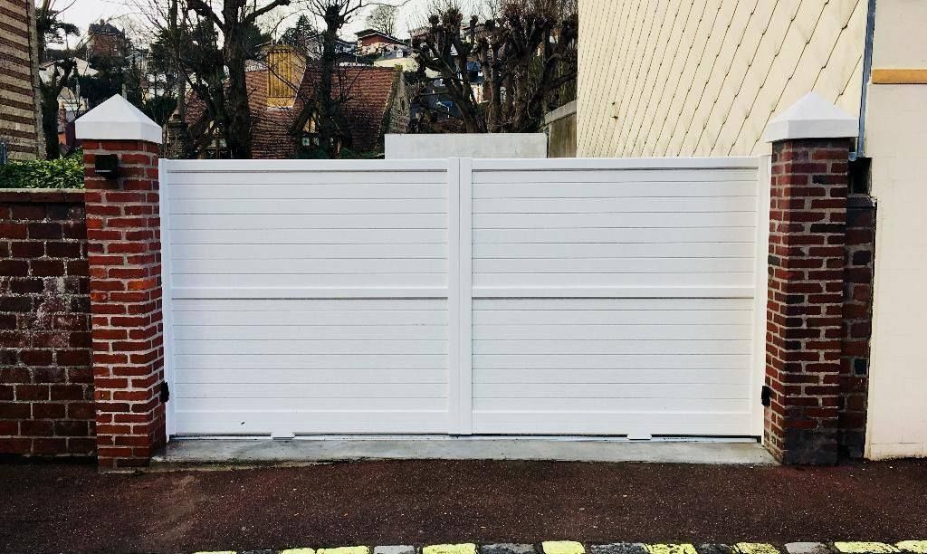 Portail coulissant blanc entre des piliers en briques rouges devant une maison