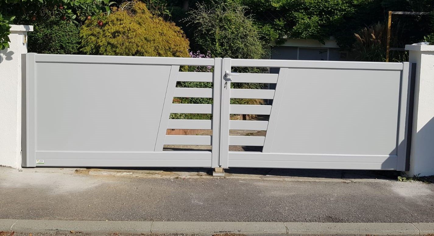 Portail d'allée moderne blanc à fentes horizontales, fermé en travers d'une allée.