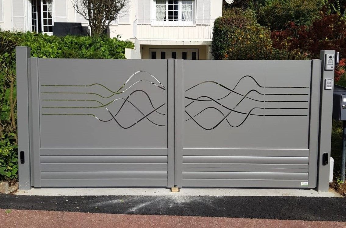 Portail d'allée en métal gris orné de vagues décoratives devant une maison et une haie