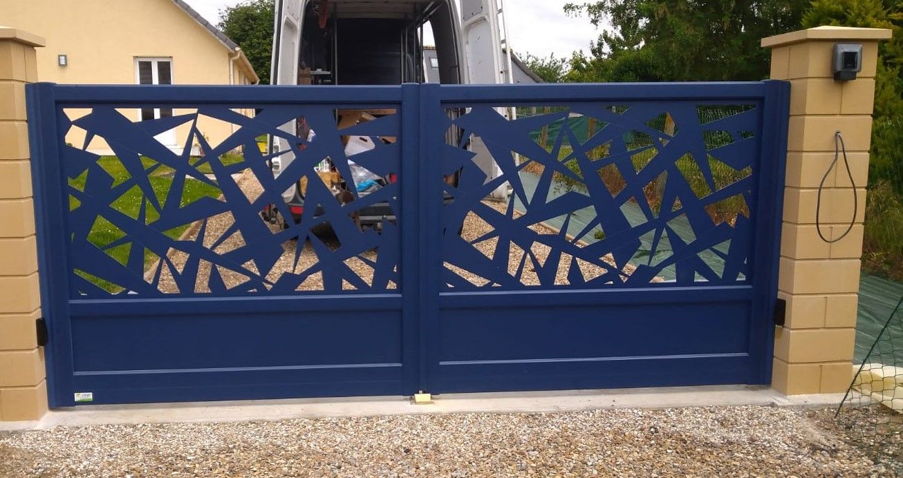 Portail en métal bleu orné de motifs ajourés abstraits entre des piliers en pierre beige devant une maison