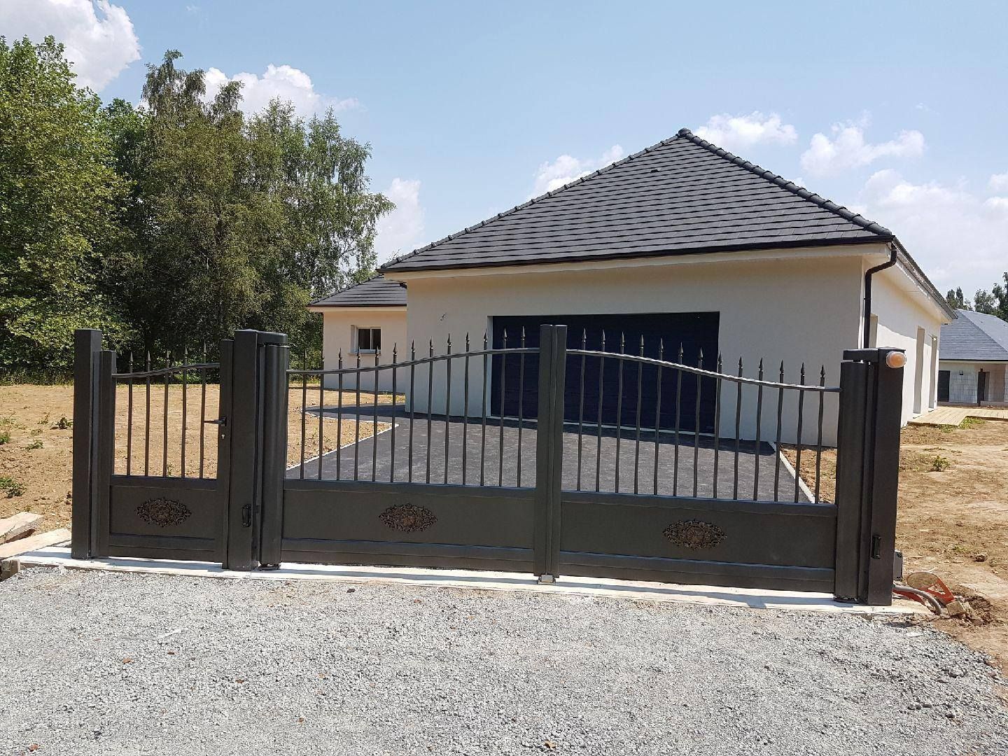 Allée privée fermée par un portail menant à une maison moderne avec un toit de tuiles et des arbres à proximité.