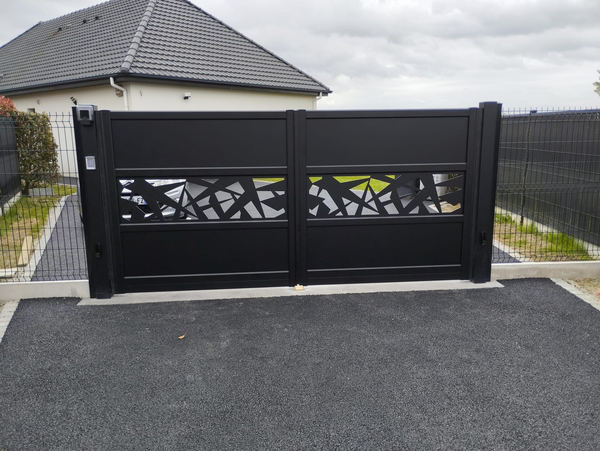 Portail d'allée moderne noir avec découpes décoratives devant une maison, vu de la rue