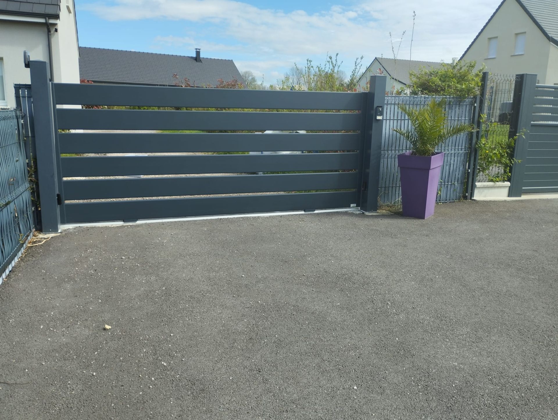 Portail d'allée gris foncé avec une jardinière violette à côté, dans une cour résidentielle