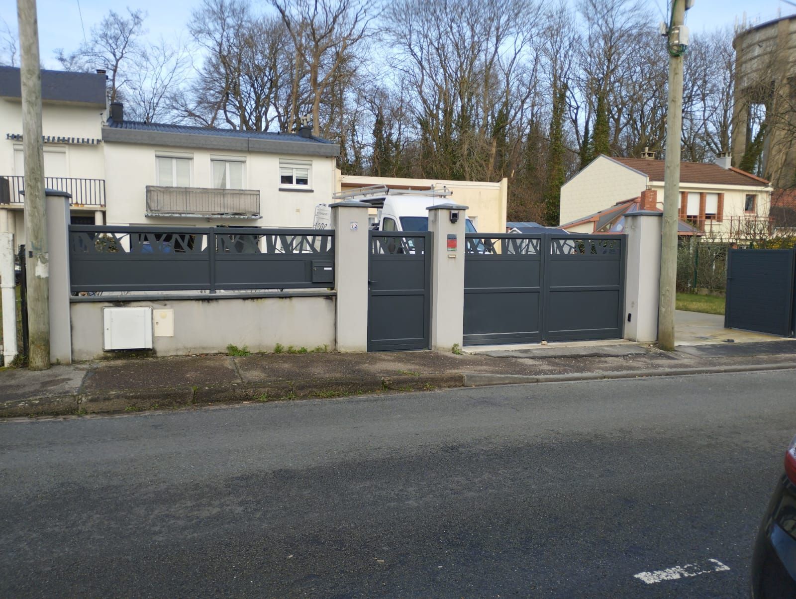 Maison d'habitation derrière une clôture et un portail gris, le long d'une rue calme.