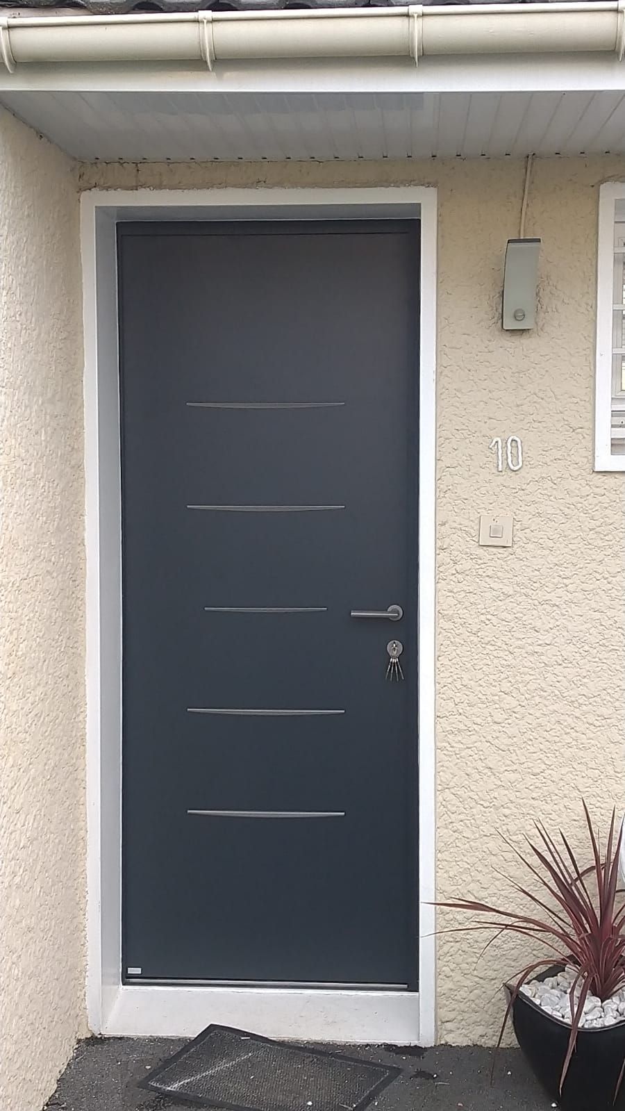 Porte d'entrée grise avec encadrement blanc sur une façade de maison en stuc beige
