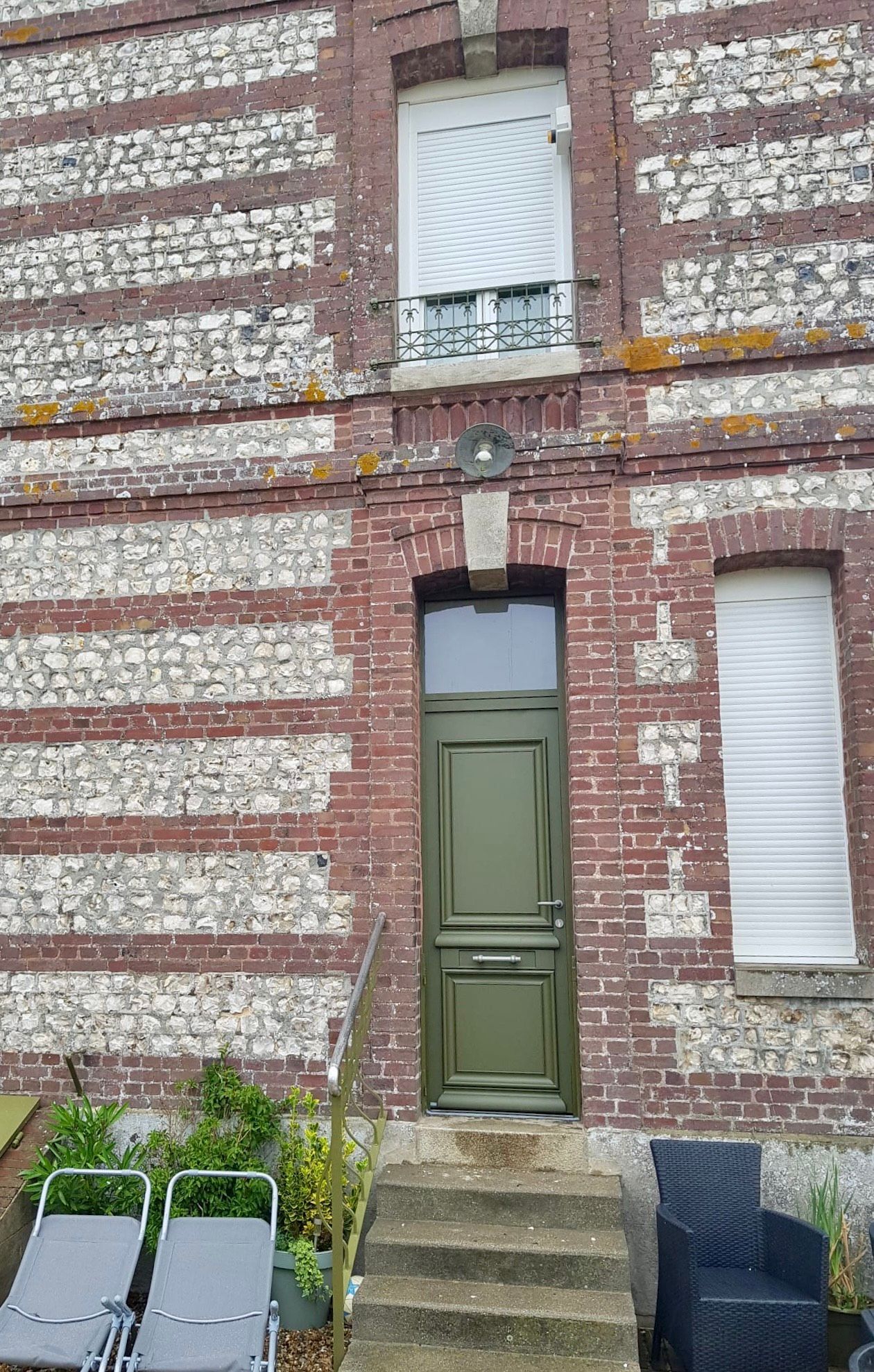 Façade de maison de ville en briques avec porte verte, marches en pierre et fenêtres aux volets blancs fermés