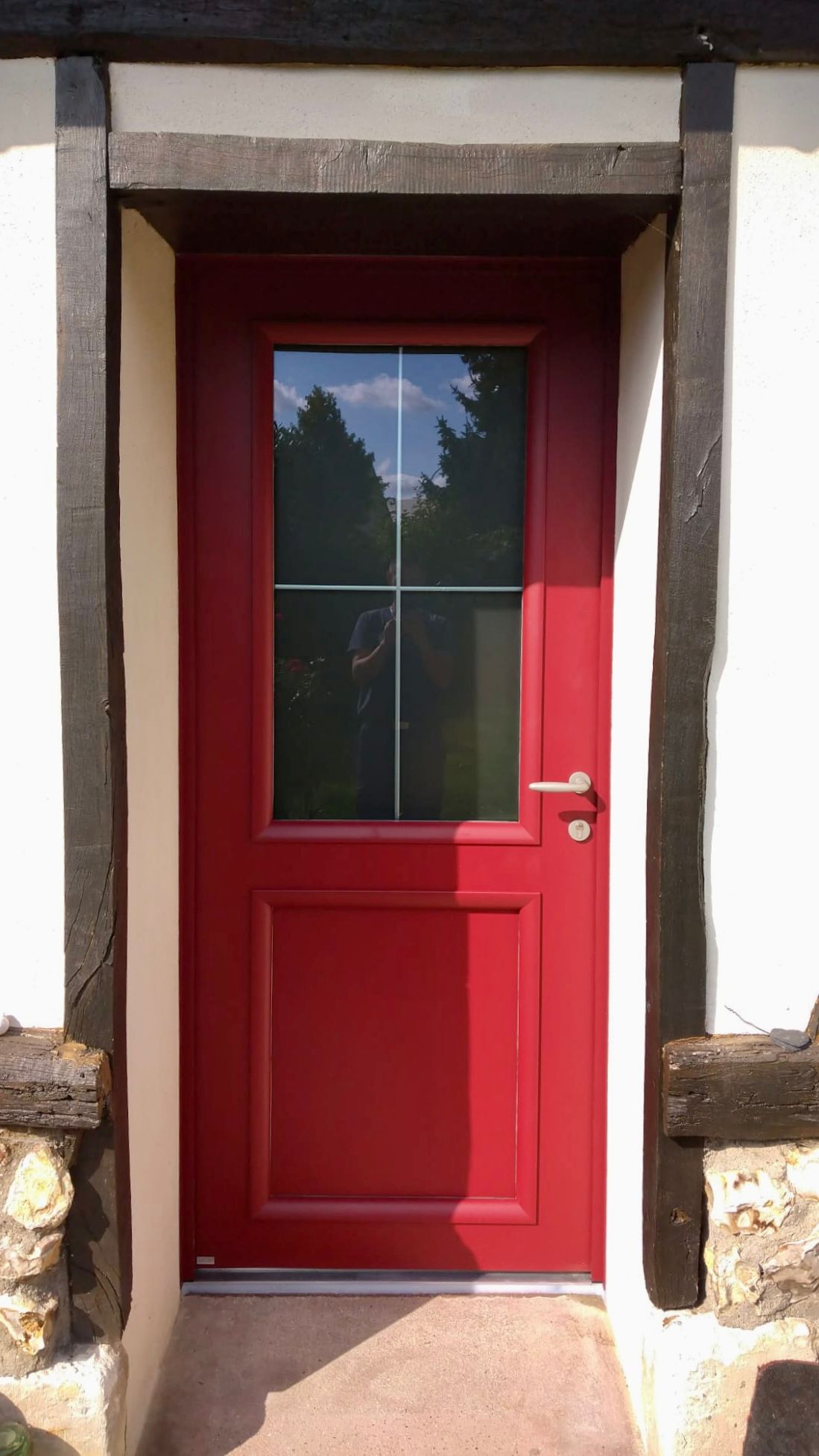 Porte d'entrée rouge avec vitre, encastrée dans un porche en stuc blanc.
