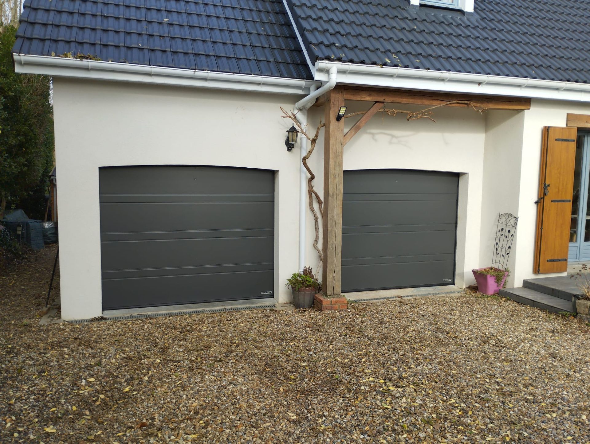 Deux portes de garage gris foncé sur une maison blanche avec allée et marches d'entrée en gravier