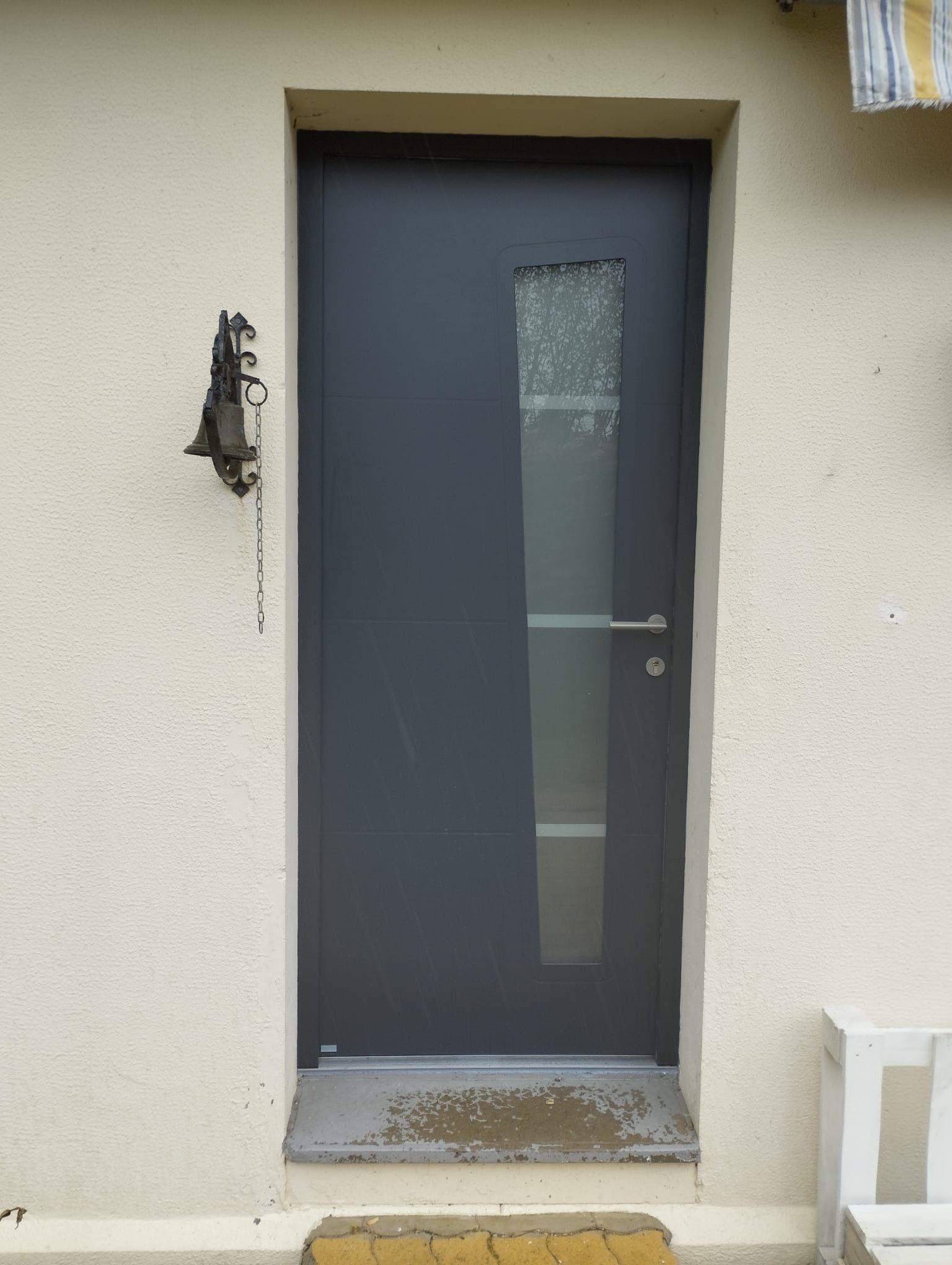 Porte d'entrée grise moderne avec panneau étroit en verre dépoli sur un mur extérieur beige