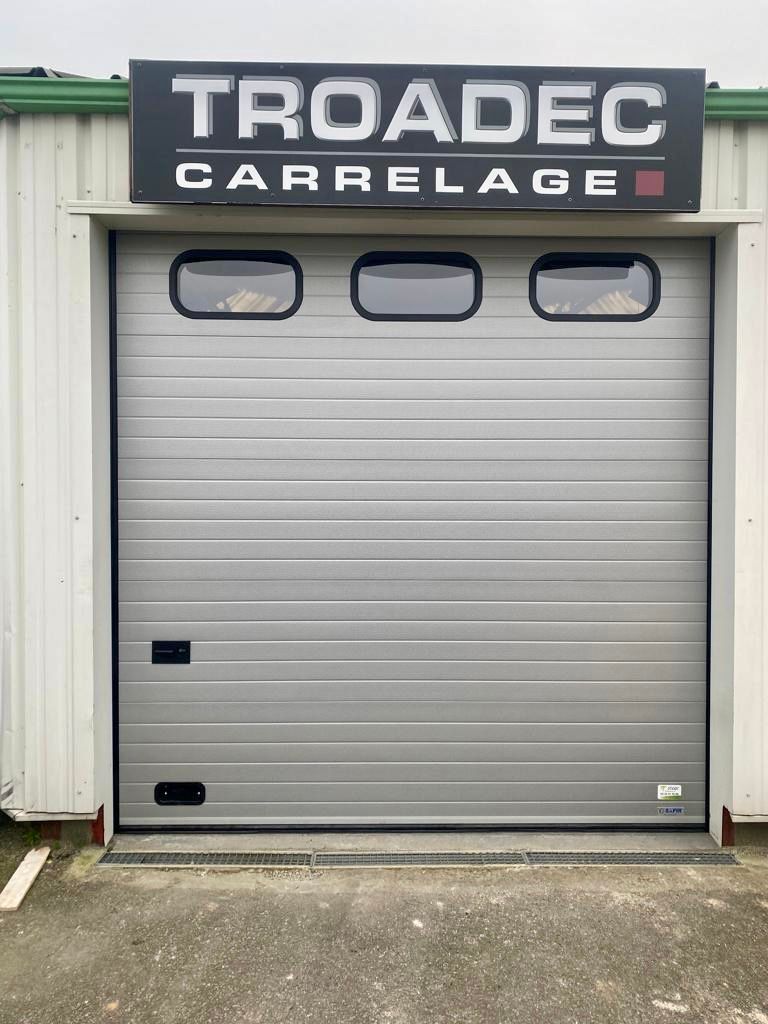 Panneau au-dessus d'une porte de garage en métal gris avec trois petites fenêtres
