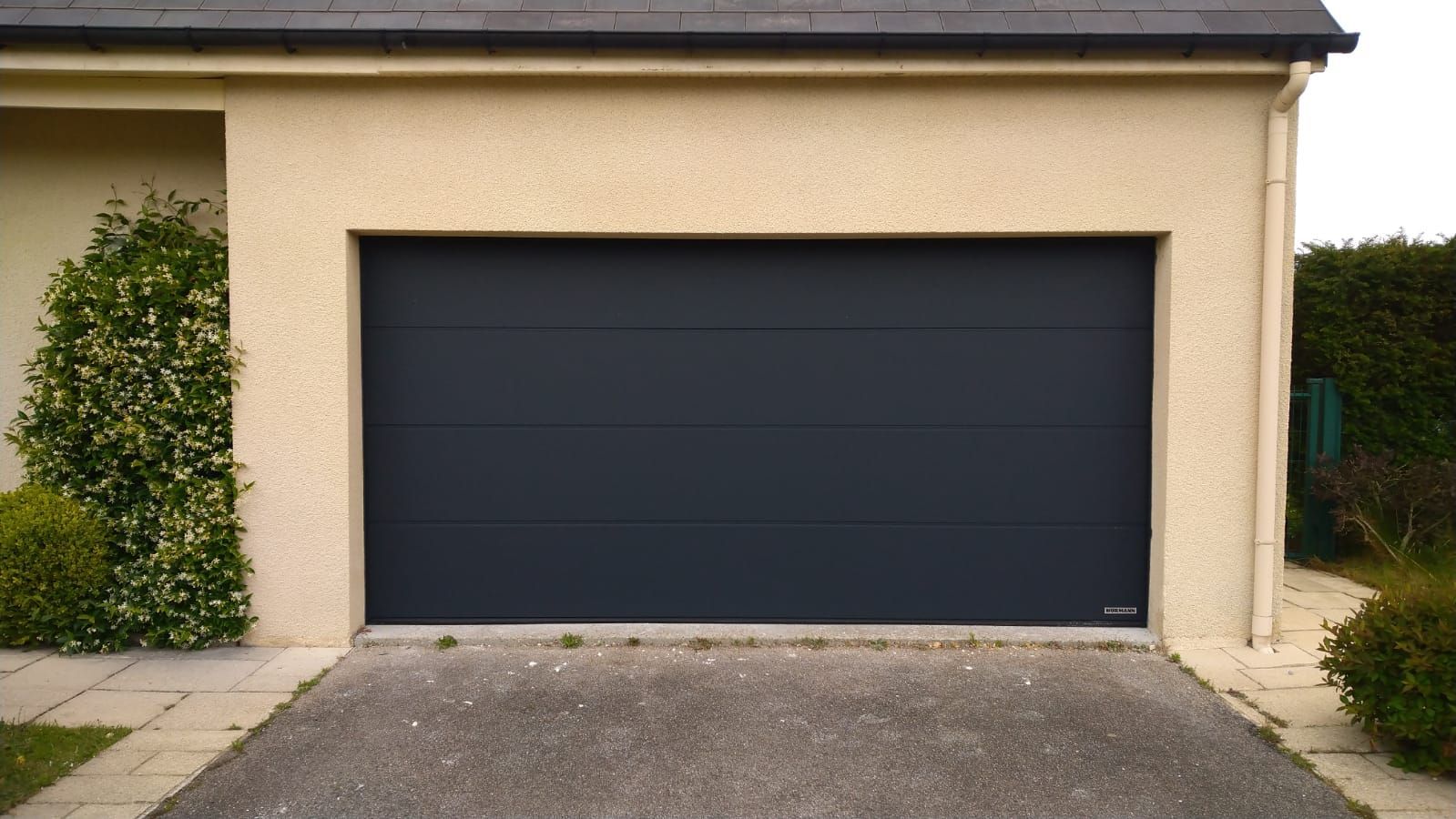 Extérieur de garage beige avec une porte fermée gris foncé et une allée pavée