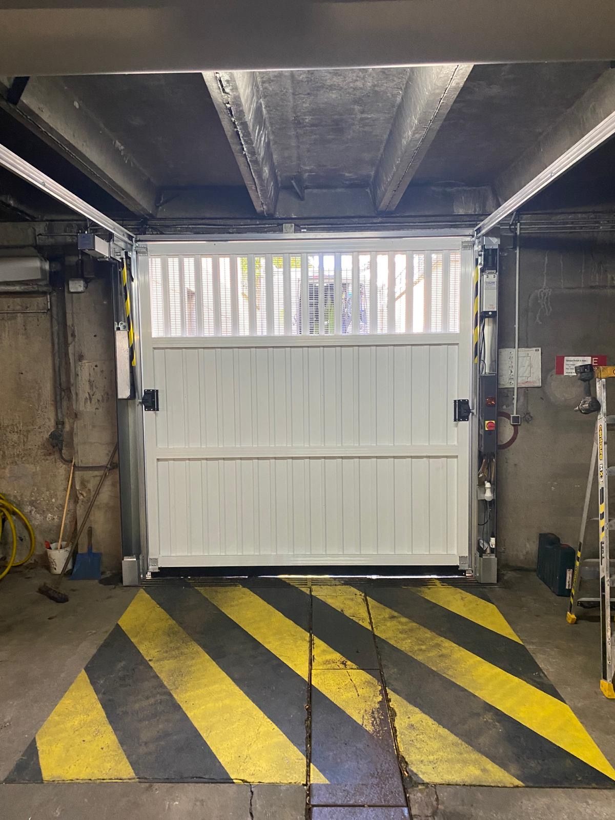 Porte de garage blanche au bout d'une place de parking avec des bandes de signalisation noires et jaunes au sol