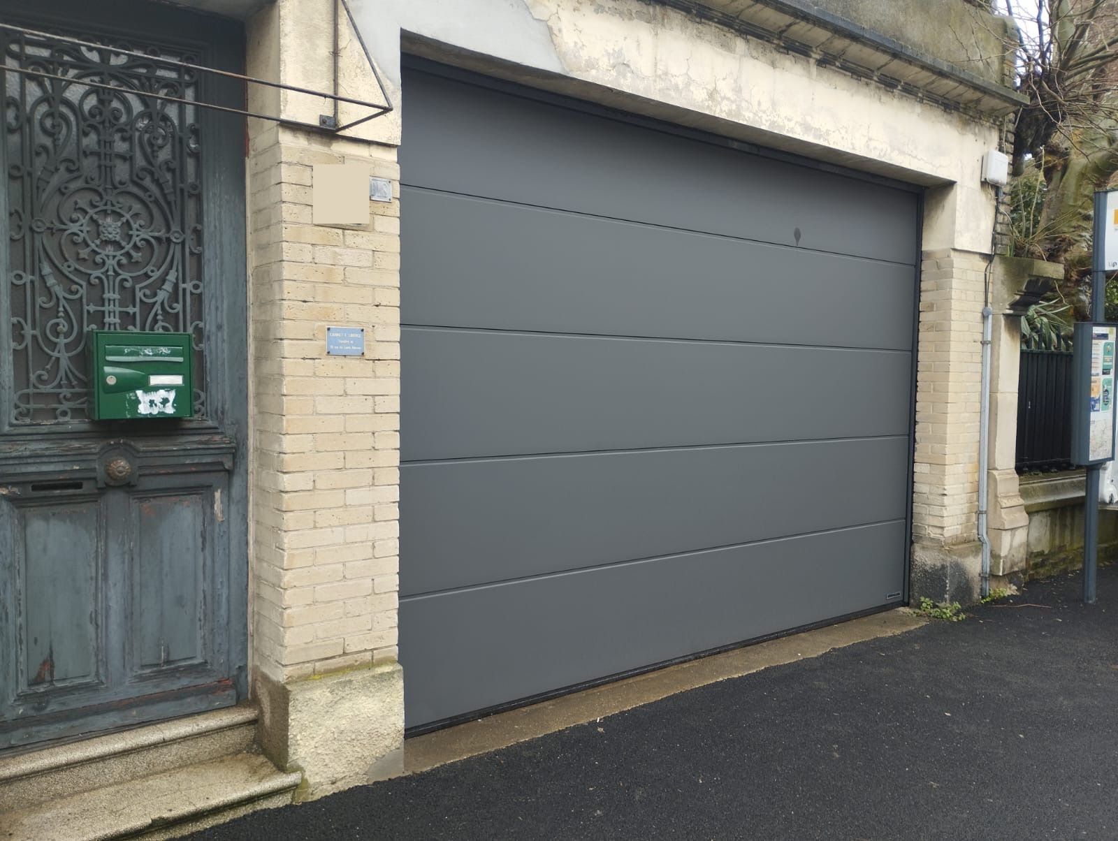 Porte de garage grise à côté d'une entrée en pierre donnant sur la rue