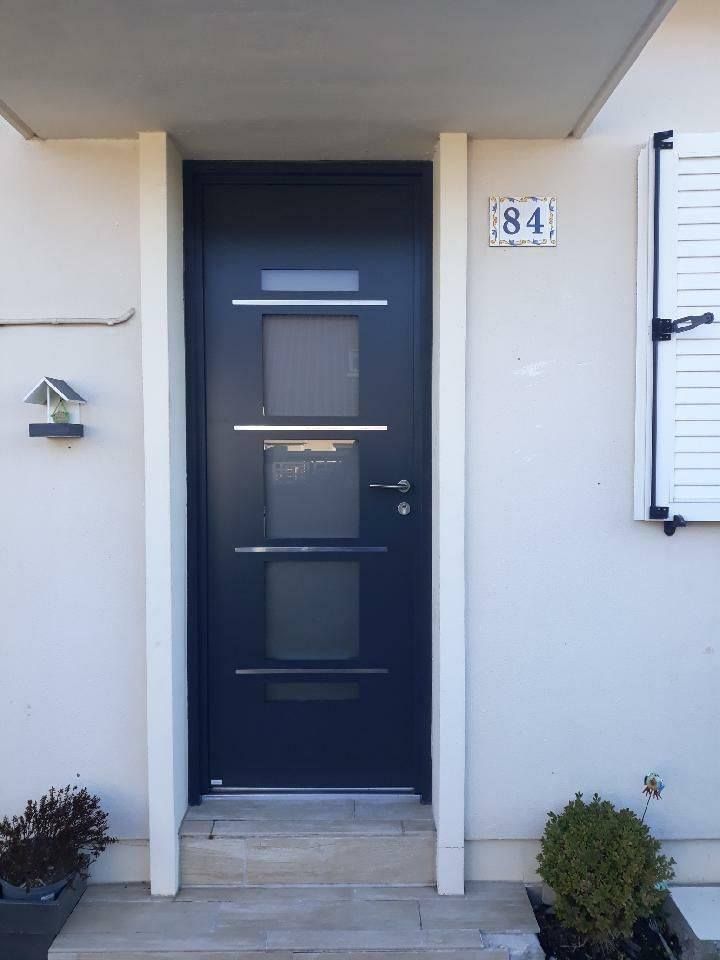 Entrée principale avec une porte bleu foncé, murs blancs et le numéro 84 au-dessus de la porte.