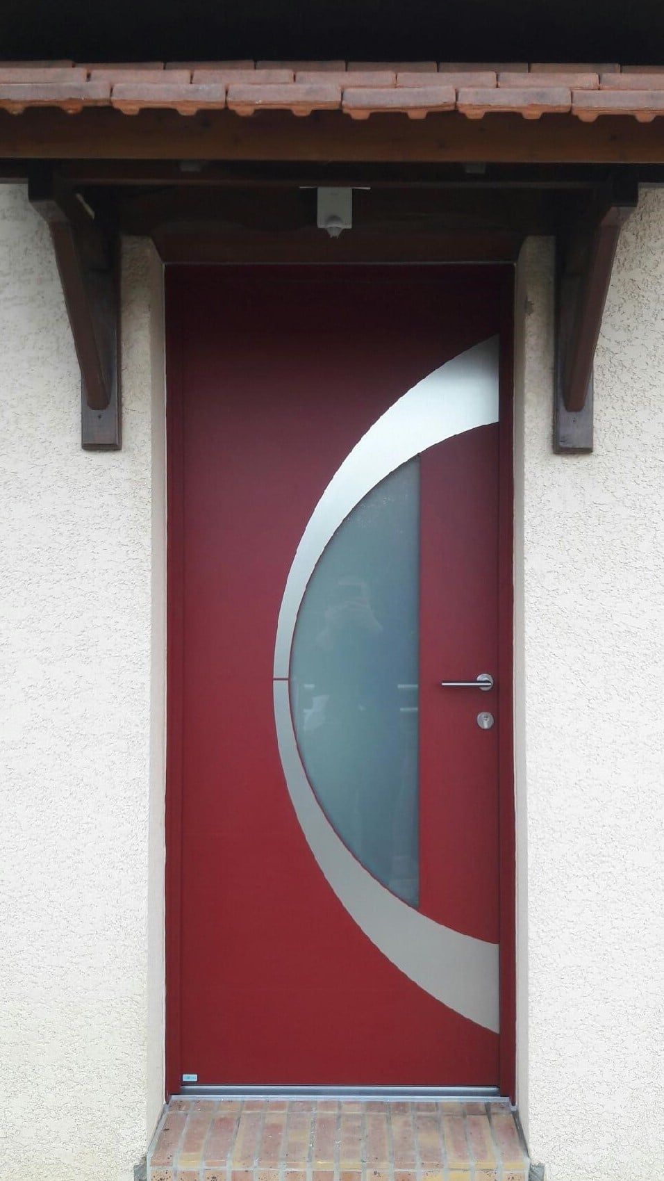 Porte d'entrée rouge avec un insert circulaire moderne en verre dépoli sous un petit porche.