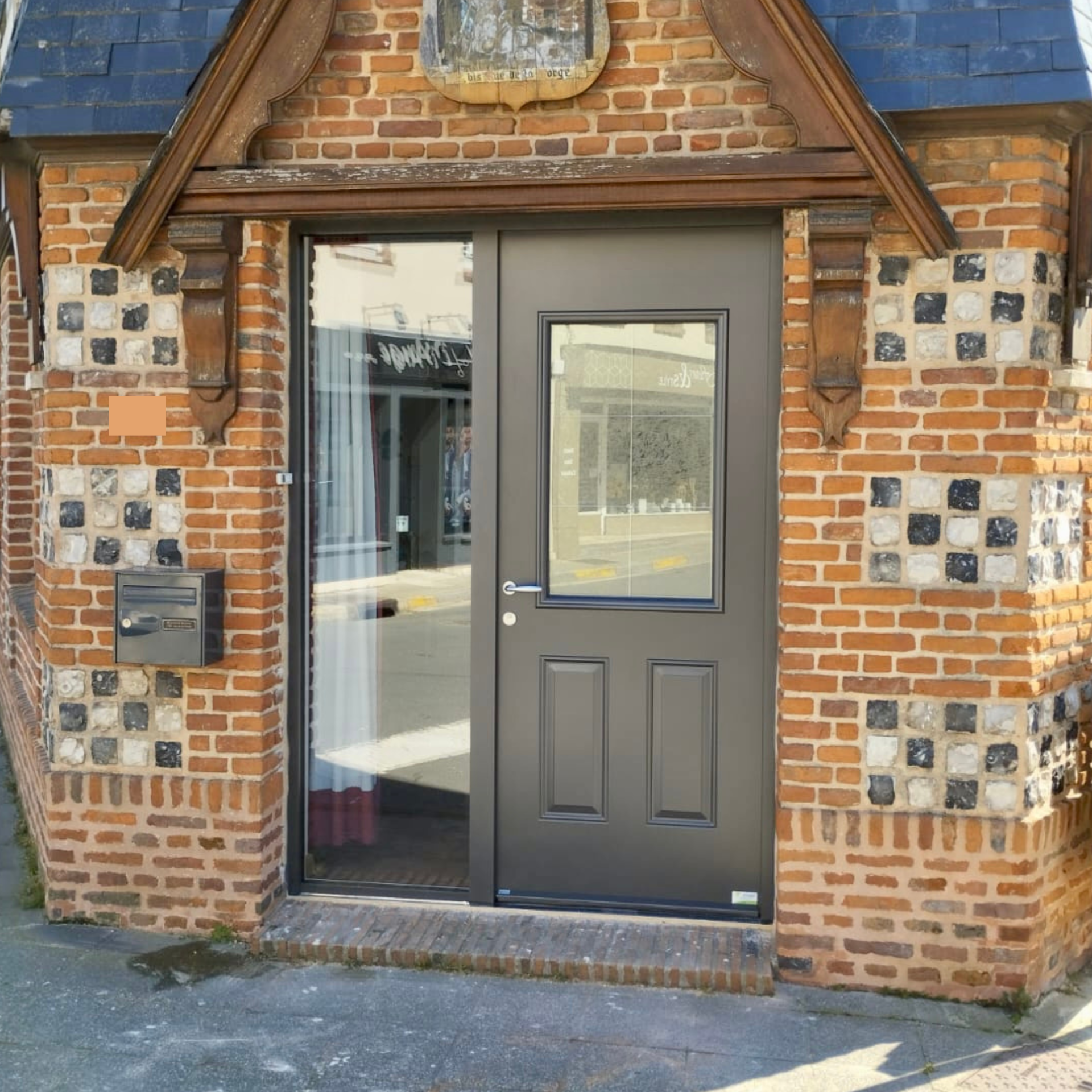 Façade en briques avec porte noire et fenêtre étroite sous un petit auvent.