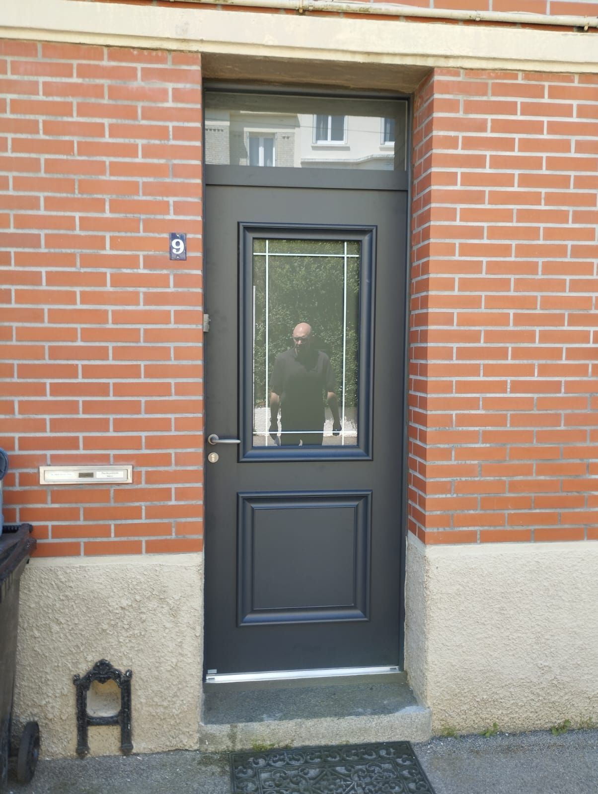 Porte d'entrée sombre avec panneau de verre encastrée dans une entrée de maison en briques rouges