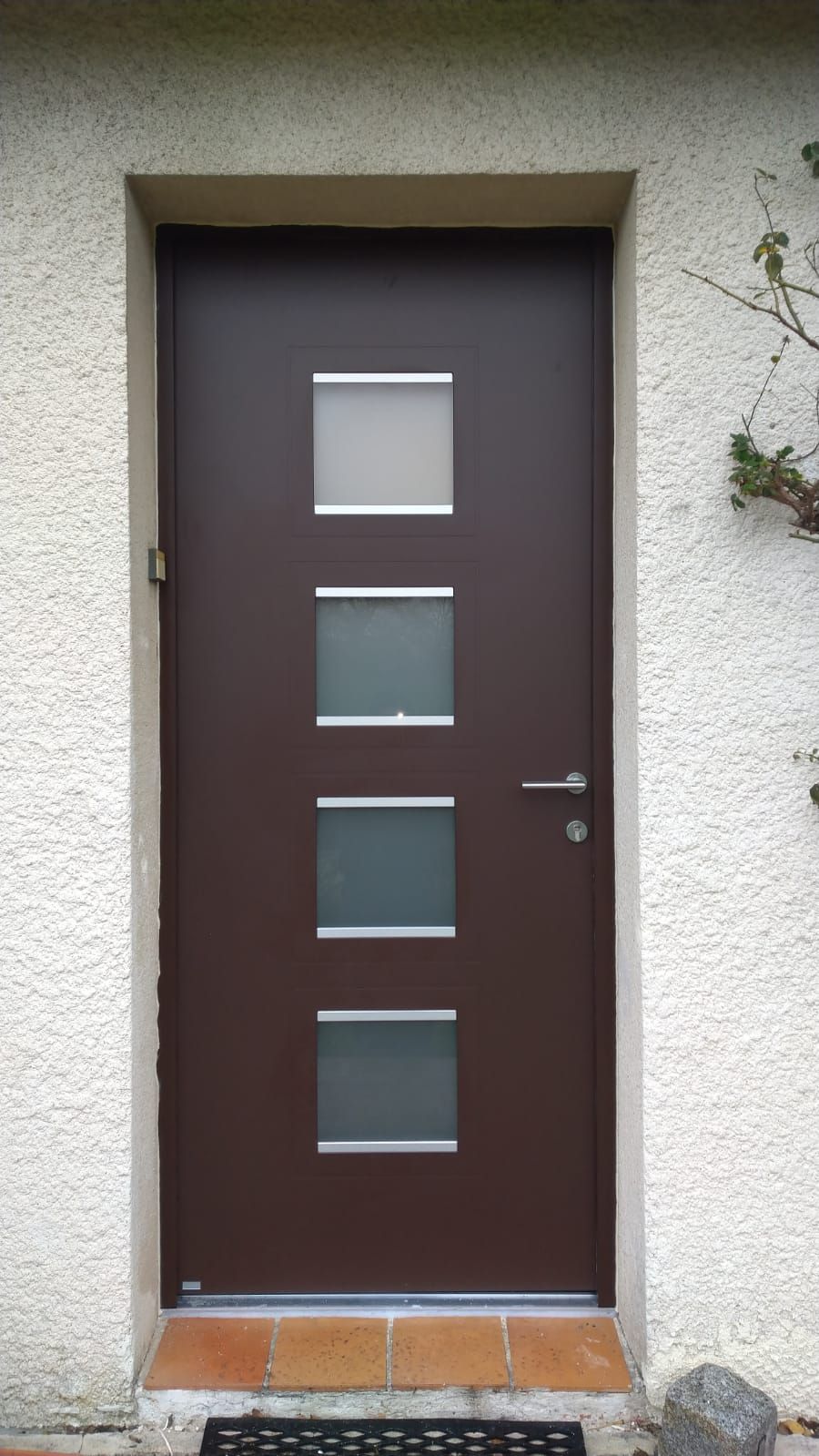 Porte d'entrée marron avec quatre panneaux de verre dépoli dans un mur en stuc blanc