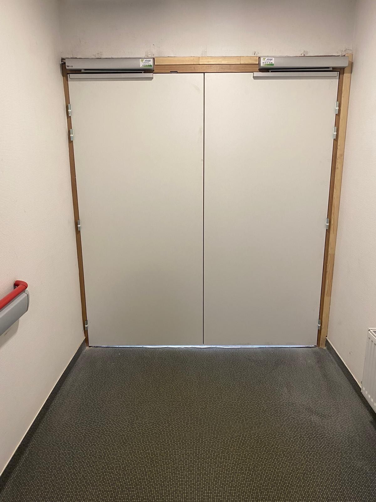 Portes d'ascenseur fermées dans un petit couloir intérieur au sol recouvert de moquette à motifs.