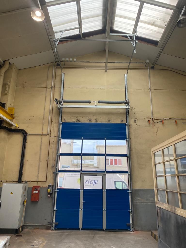 Intérieur d'entrepôt industriel avec porte sectionnelle bleue et haut plafond vitré.