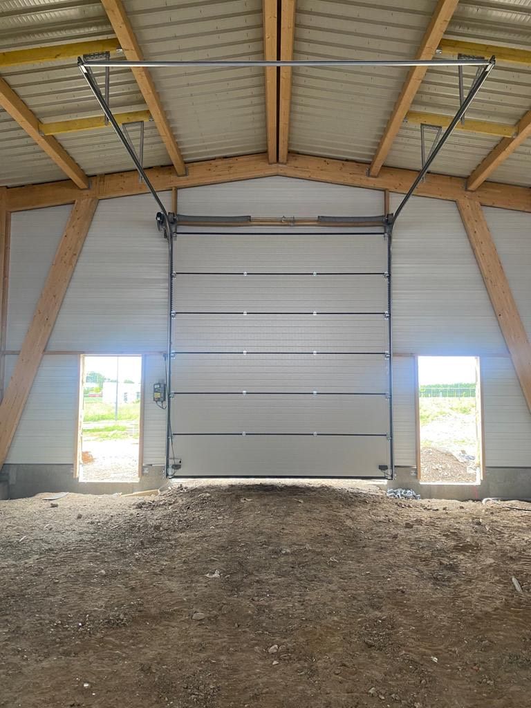 Intérieur d'une grange avec une grande porte de garage blanche sectionnelle et un sol en terre battue.