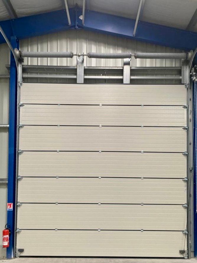 Porte de garage industrielle beige fermée à l'intérieur d'un bâtiment métallique à encadrement bleu.