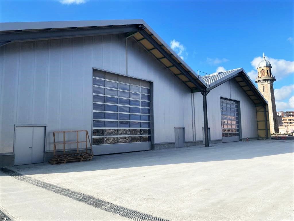 Entrepôt industriel avec des finitions bleues, de grandes portes de garage et une haute tour en arrière-plan.