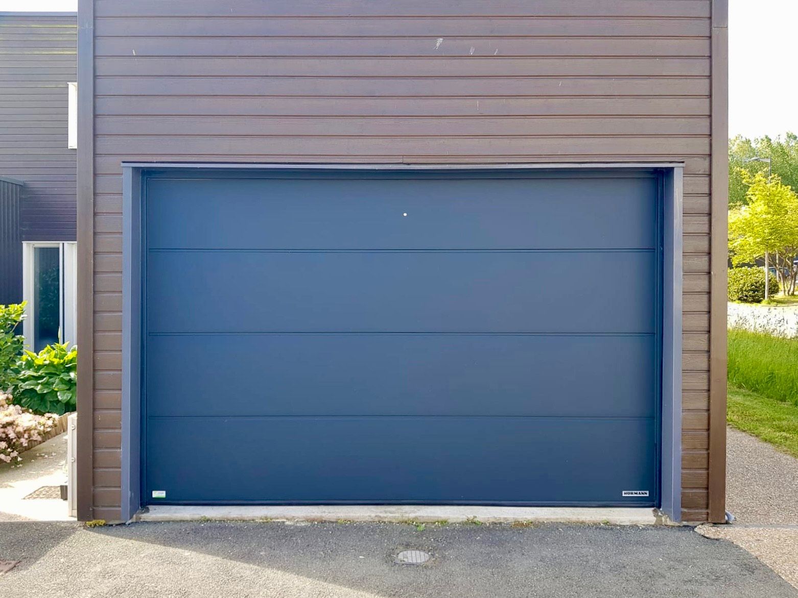 Porte de garage bleue sur une façade de maison moderne marron, avec une petite allée pavée
