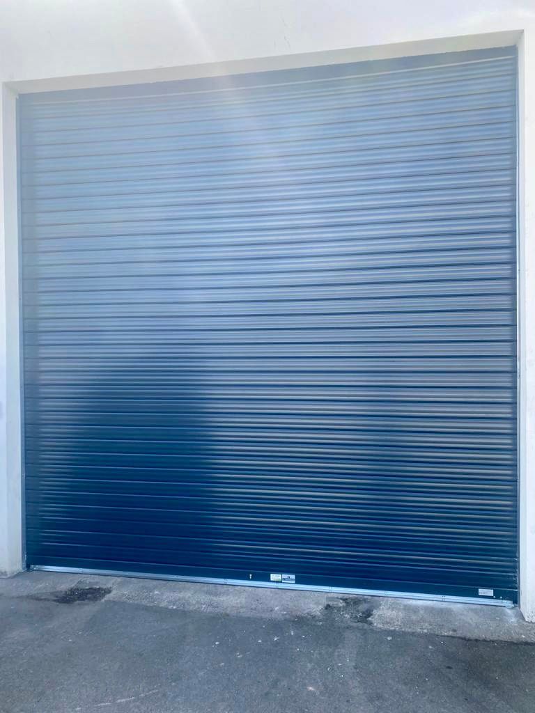 Porte de garage sectionnelle en tôle ondulée bleue dans une ouverture de mur en béton