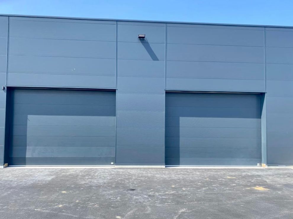 Façade bleue d'un bâtiment industriel avec deux portes de garage fermées et un devant pavé