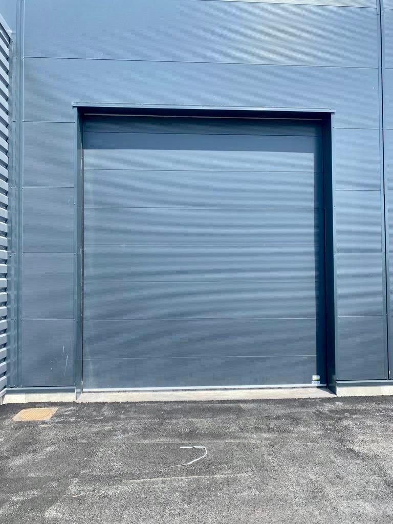 Porte de garage enroulable grise fermée sur un bâtiment industriel bleu.