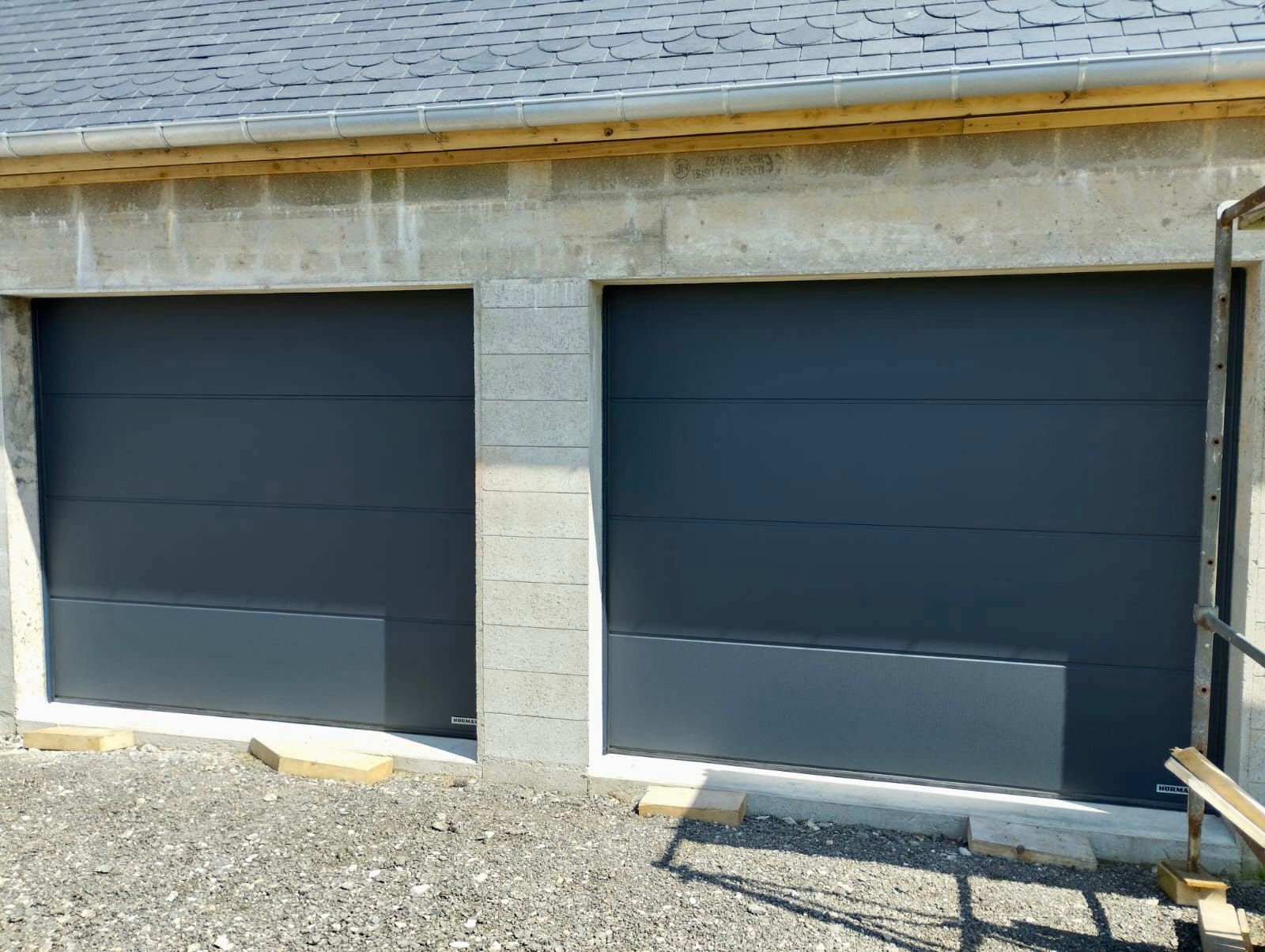 Deux portes de garage bleu foncé dans une façade en pierre avec une allée de gravier devant