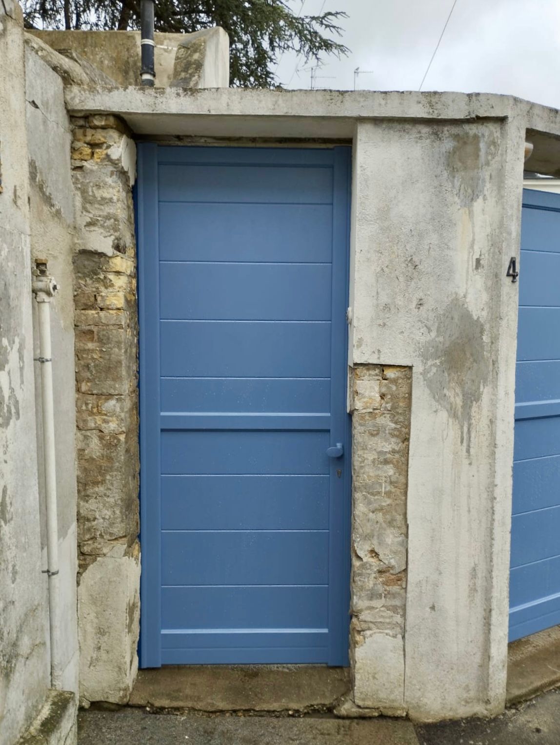 Porte bleue encastrée dans un mur de pierre patiné, avec un petit pilier de pierre à côté.