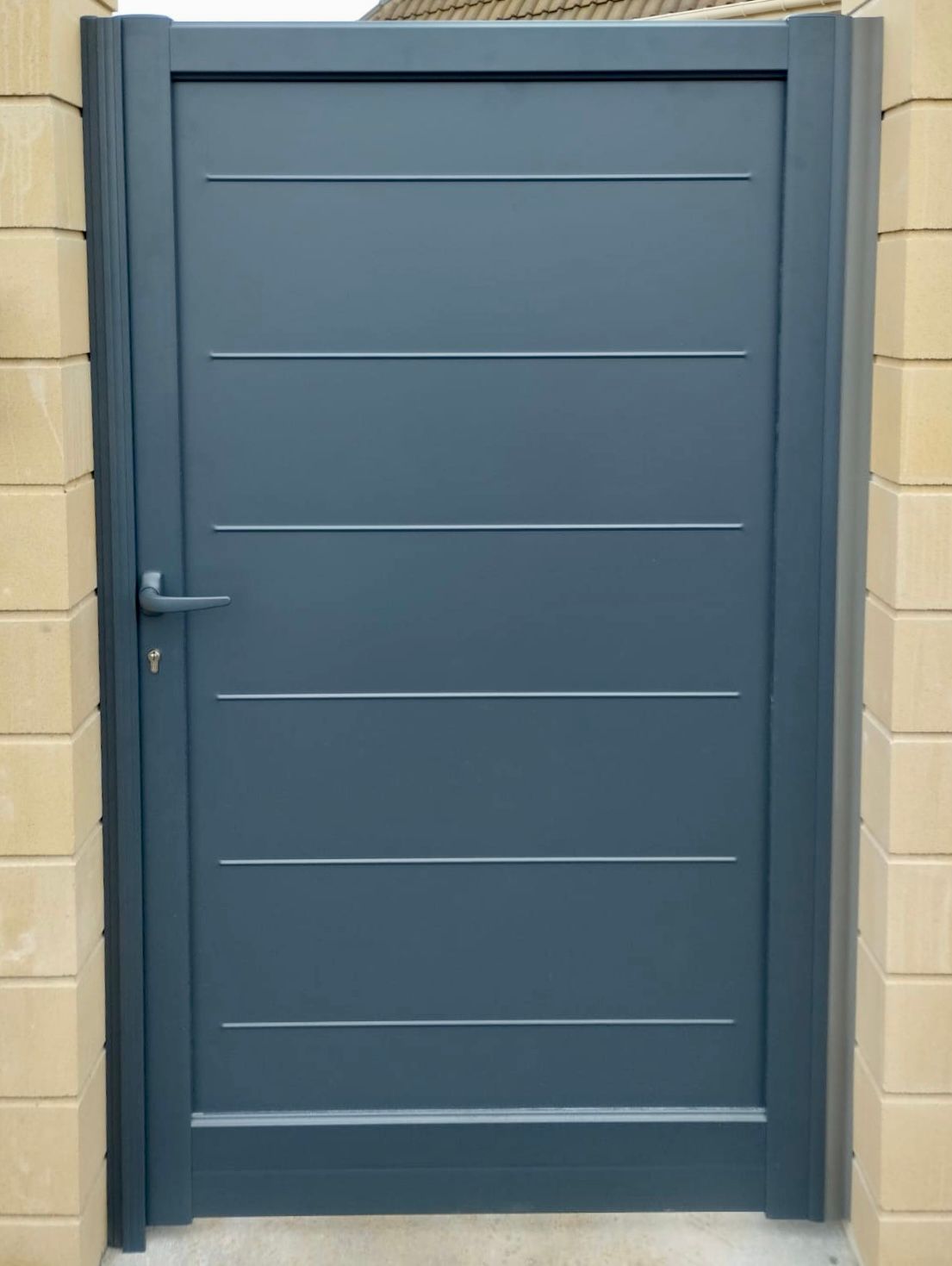 Porte bleu-gris à panneaux horizontaux encastrée dans un mur en parpaings beiges