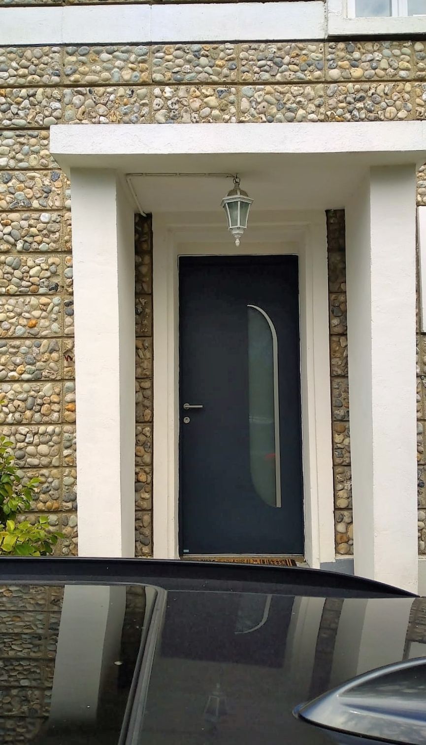 Entrée principale avec une porte sombre, des moulures blanches, une façade en pierre et un capot de voiture au premier plan.