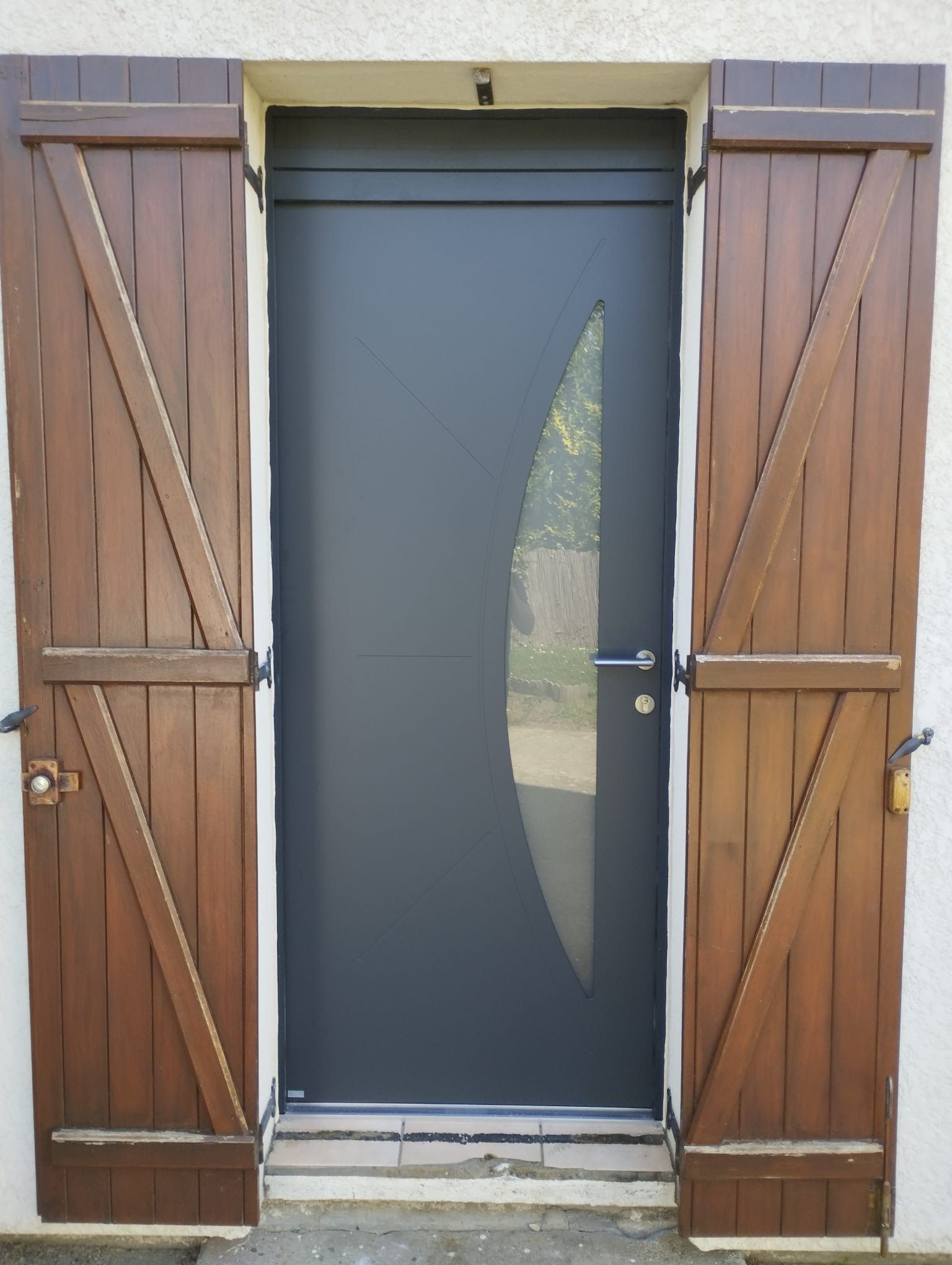 Entrée principale avec porte en verre foncé et volets en bois de chaque côté